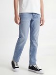 Jongen in wit T-shirt en lichtblauwe jeans, zittend. Draagt zwarte sneakers met witte zolen.