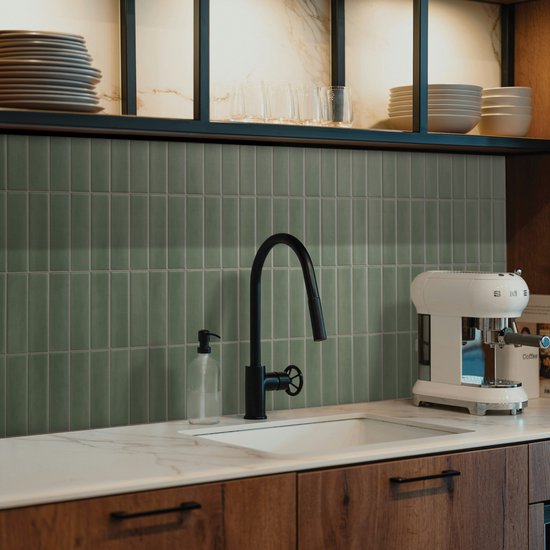 Mosgroene, verticale tegels bedekken de achterwand van een keuken met een witte wasbak en een witte koffiemachine.