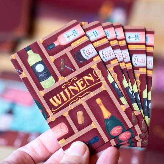 Een hand houdt een stapel kaarten vast met afbeeldingen van wijnflessen, kurkentrekkers en kurken in een kast-design. De titel 'WIJNEN' staat erop.