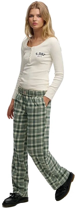Model in een wijde groene plaid broek met een crèmekleurig shirt en zwarte schoenen.