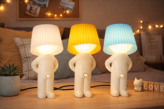 Drie lampjes in de vorm van een mannetje, met witte, gele en blauwe kap, op een houten tafel.