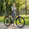Vrolijke vrouw met grijze elektrische fiets in een park, zonnige dag.