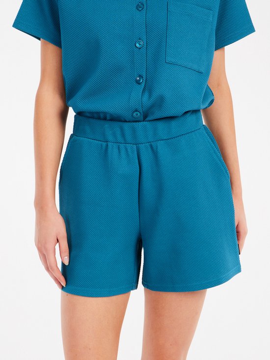 Close-up van een turquoise korte broek met elastische tailleband.