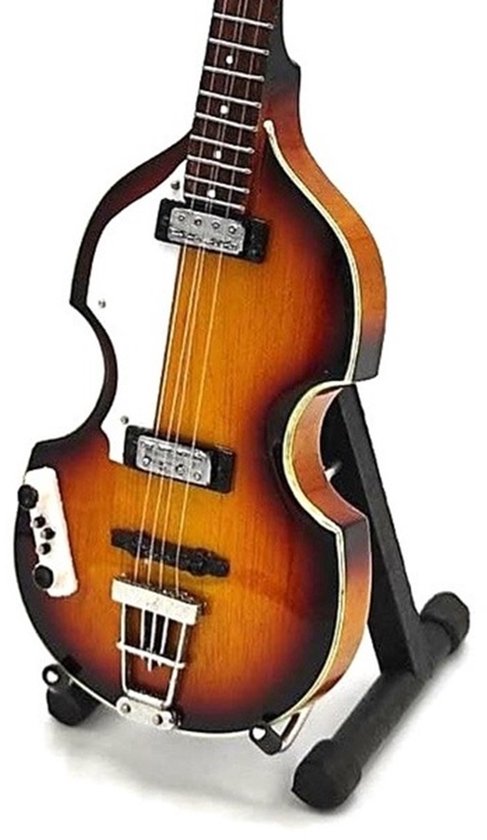 Guitare basse miniature en forme de violon, sunburst avec pickguard blanc, sur un support.