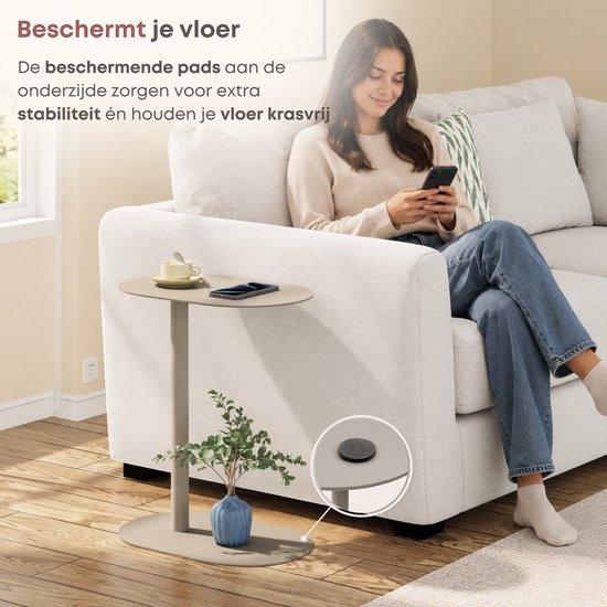 Taupe bijzettafel met beschermende pads aan de onderkant. Een vrouw zit op een bank, telefoon in de hand.