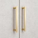 Twee matte messing handgrepen met gouden kleur op lichtgrijze, betonnen kasten.