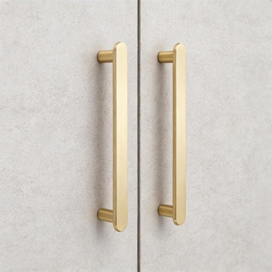 Twee matte messing handgrepen met gouden kleur op lichtgrijze, betonnen kasten.