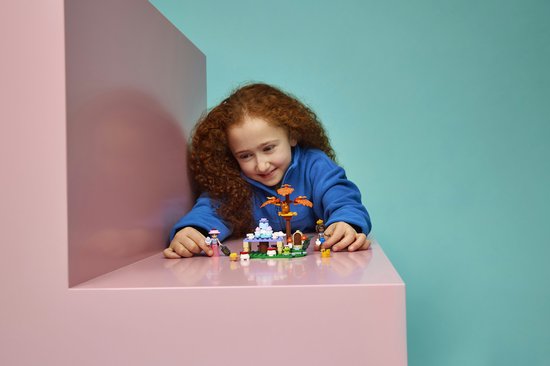 Meisje met krullend rood haar speelt met LEGO Friends bosfeest speelset op een roze en blauwe achtergrond.