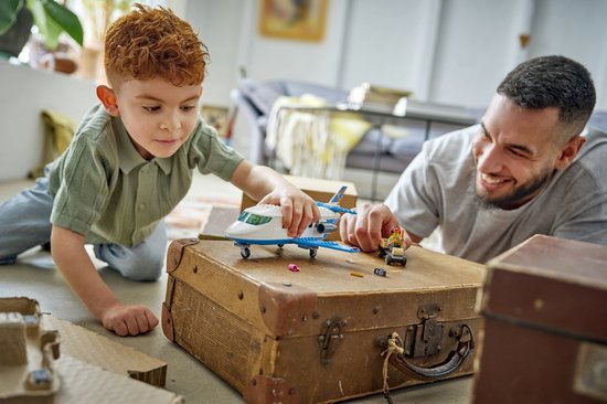 Vader en zoon spelen met een wit en blauw LEGO vliegtuig op een bruine koffer.