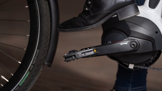 Pied dans une chaussure noire sur une pédale de vélo noire avec réflecteur orange, montée sur un entraînement de vélo électrique Bosch.
