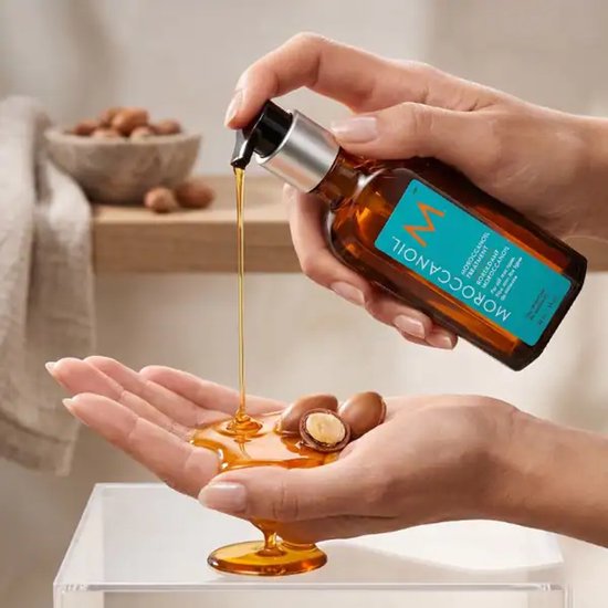 Handen doseren Moroccanoil Treatment in een handpalm, met argannoten.