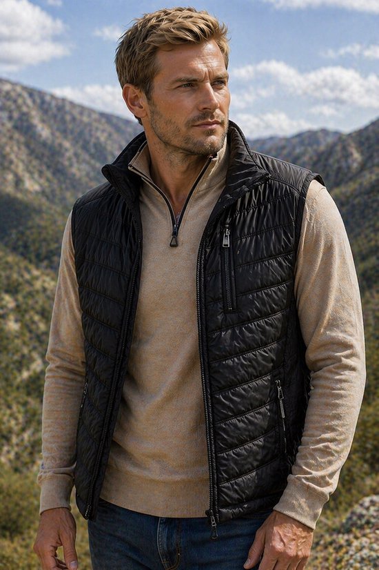 Man met zwarte Bjørnson bodywarmer met visgraatmotief, beige trui en spijkerbroek, in de bergen.