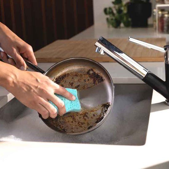 Mains frottant une poêle avec une éponge à récurer bleue.