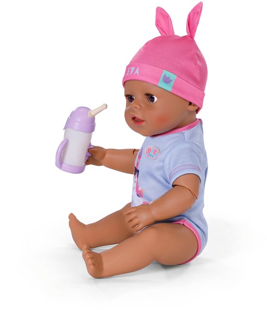 BABY born pop Eva zit, drinkt uit paarse fles, draagt blauw romper met eenhoorn en roze konijnenmuts.