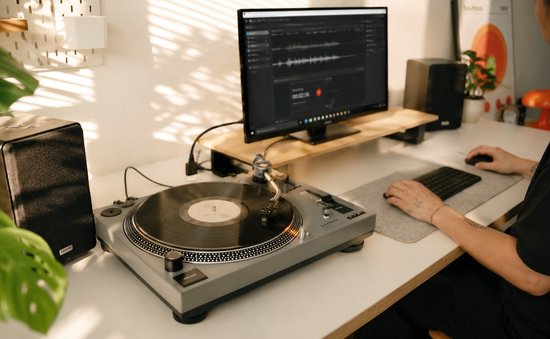 Grijze draaitafel met draaiende plaat, naast een computer waarop geluid bewerkt wordt.