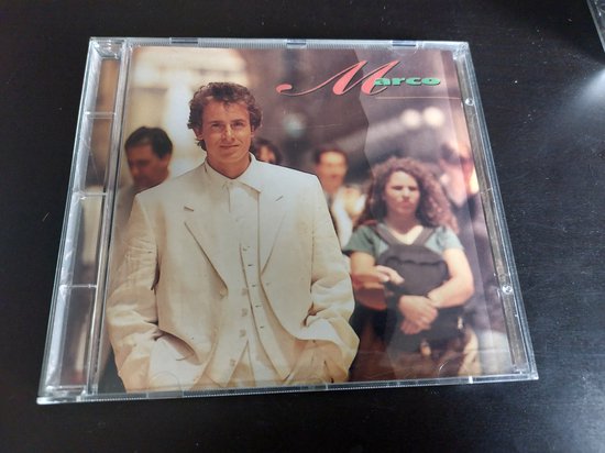 CD-hoes met Marco Borsato in een wit pak. Hij staat op een straat met mensen op de achtergrond. De naam 'Marco' staat rechtsboven.