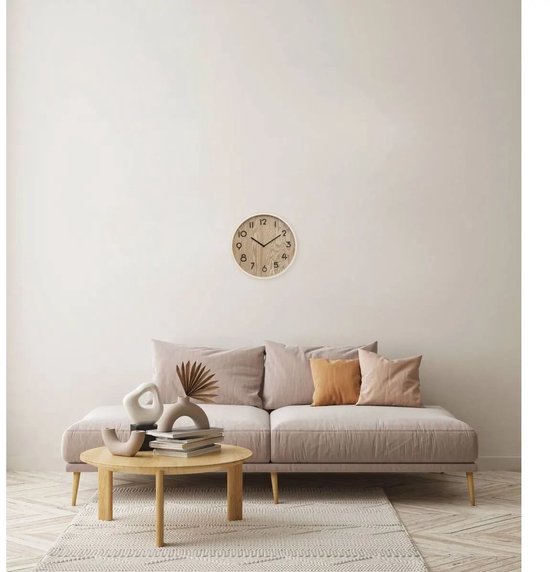 Ronde beige houten klok met zwarte cijfers, hangend boven een bank.