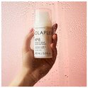 Hand houdt witte OLAPLEX Nr. 8 fles vast tegen een roze achtergrond met waterdruppels.