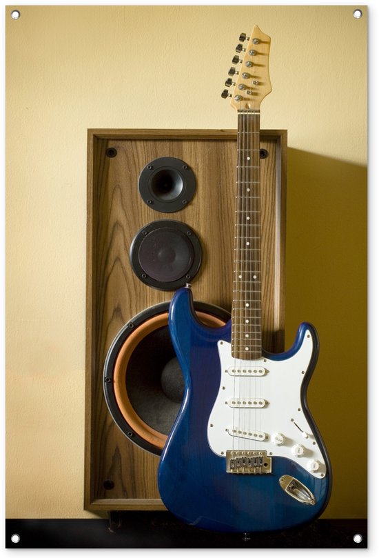 Blauwe elektrische gitaar met witte slagplaat, voor een houten luidspreker tegen een gele muur.