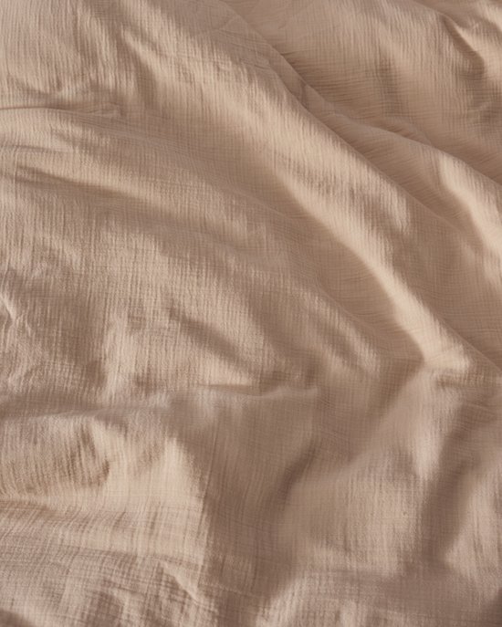 Close-up van een zachtroze dekbedovertrek met kreukelige textuur.