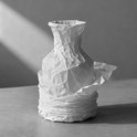 Een vaas, verpakt in wit kreukpapier, met dramatische schaduwen.