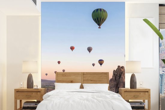 Luchtballonnen varen boven een rotsachtig landschap bij zonsopgang, boven een bed.