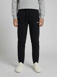 Jongen draagt een grijze sweater en een zwarte joggingbroek met wit 'JJR.' logo.