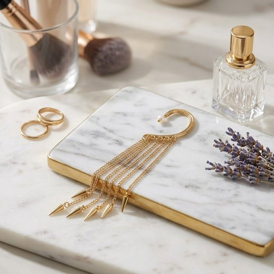 Goudkleurige ear cuff met pareldetail en meerdere kettingen met puntige hangers, liggend op een marmeren plateau met gouden rand.