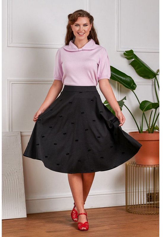 Femme portant un pull rose à manches bouffantes et une jupe cercle noire à imprimé cerises. Elle porte des sandales rouges.