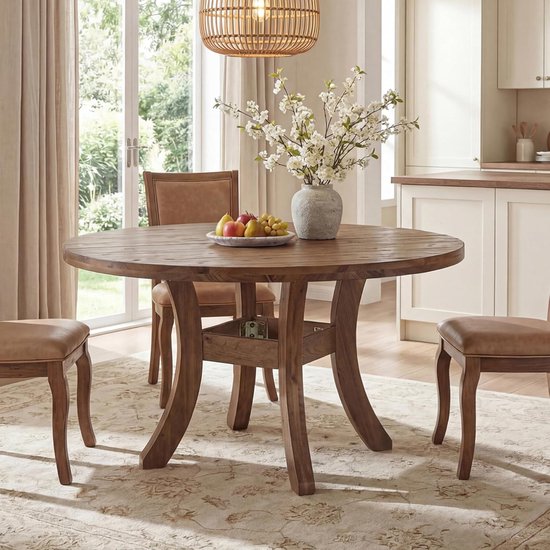 Ronde, houten eettafel met leren stoelen, gedekt voor vier personen met fruit en bloemen in een vaas.