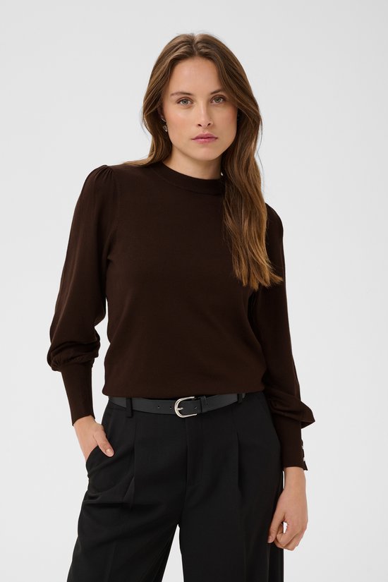 Model in bruine trui met pofmouwen en zilverkleurige knopen, gecombineerd met zwarte broek.