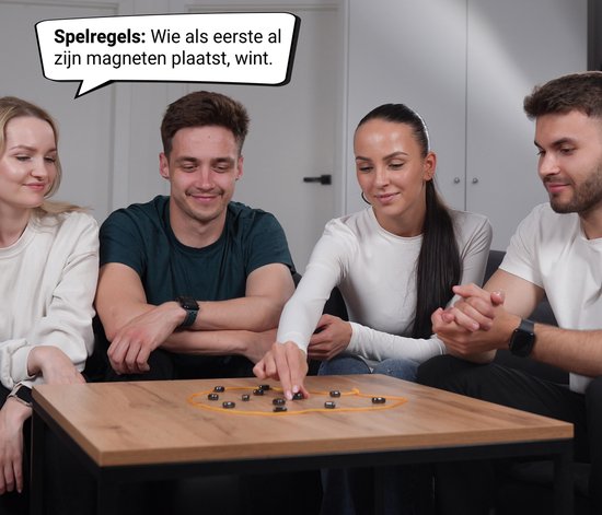 Vier vrienden spelen een spel met magneten op een tafel. De tekstballon zegt: 'Spelregels: Wie als eerste al zijn magneten plaatst, wint.'