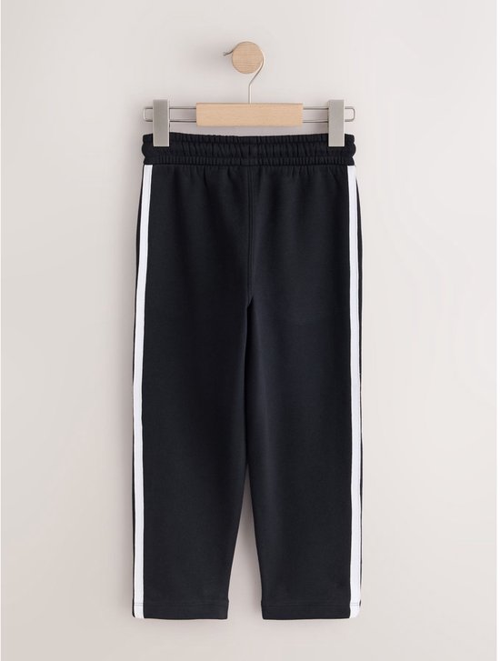 Zwarte joggingbroek voor jongens met witte strepen aan de zijkant, hangend aan een kledinghanger.