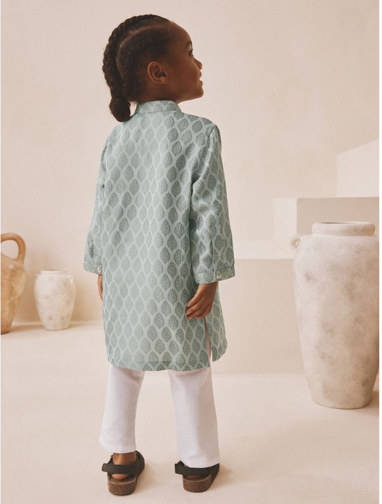 Achteraanzicht van een jongen in een lichtgroene kurta met bladpatroon en een witte broek.