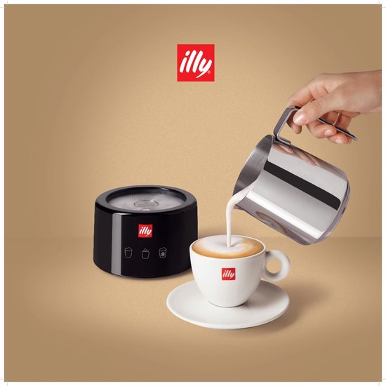 Hand giet melk uit een RVS melkkan in een witte Illy kop. Naast staat een zwarte Illy melkopschuimer met het Illy logo.