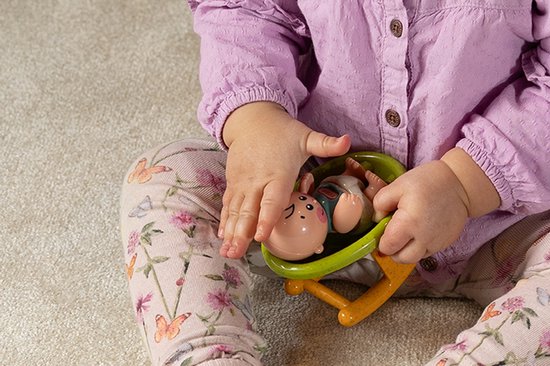Baby in paars hemd en met vlinders en bloemen bedrukte legging houdt een Tolo BIO baby met wieg speelgoed vast.