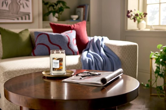 Een Amber & Sandalwood Yankee Candle in een grote pot staat op een bijzettafel in een woonkamer.