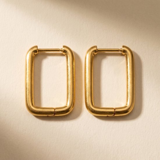 Gouden, rechthoekige oorringen op een gebroken witte achtergrond.