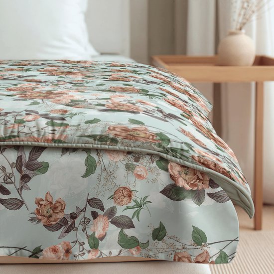 Detail van een lichtgroen dekbed met een print van roze en oranje bloemen en groene bladeren.