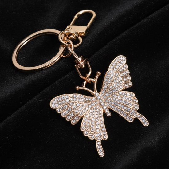 Gouden sleutelhanger met vlinderhanger bezet met strass, op zwarte stof.