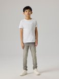 Jongen draagt een grijze, aansluitende jeans met een wit t-shirt en witte sneakers.