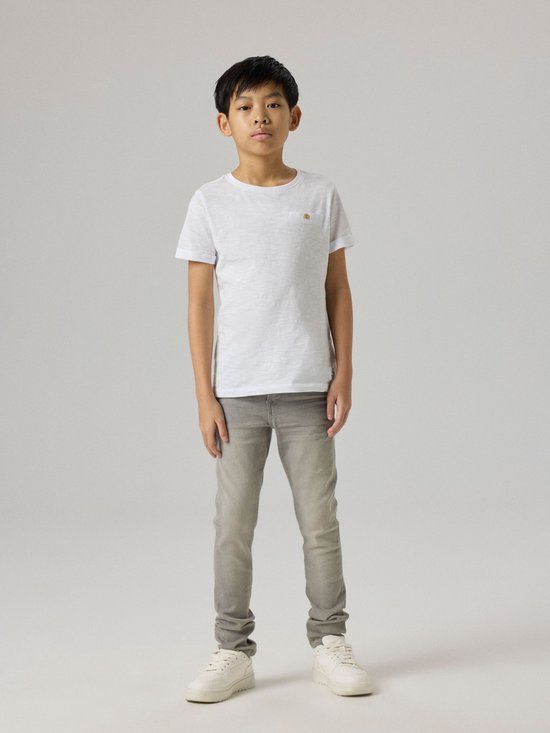 Jongen draagt een grijze, aansluitende jeans met een wit t-shirt en witte sneakers.