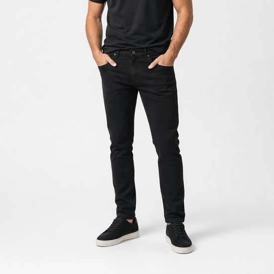 Man met zwarte skinny broek en zwarte sneakers, handen in zakken.