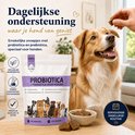 Bruine hond zittend naast een verpakking 'Probiotica + Prebiotica voor Honden', een bakje brokjes, met een hand die een brokje geeft.