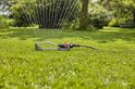 Grijze zwenksproeier met oranje details, waterstralen spuitend op groen gras.
