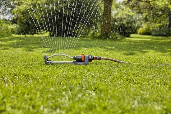 Grijze zwenksproeier met oranje details, waterstralen spuitend op groen gras.