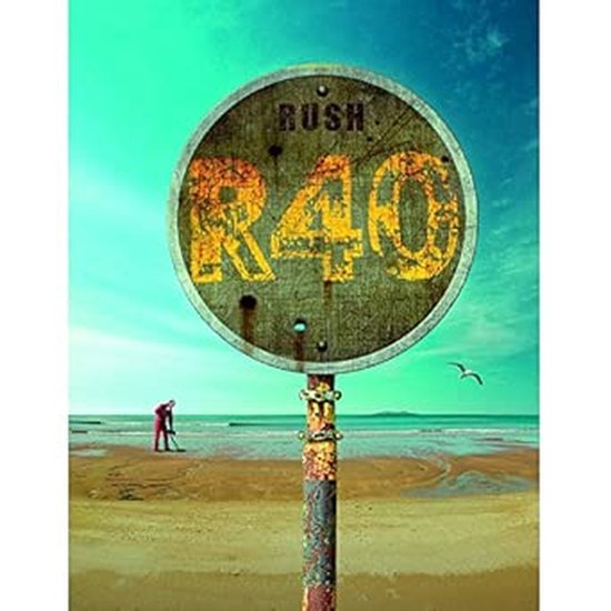 Een roestige ronde "R40"
wegwijzer op een strand met op de achtergrond de zee en een persoon die in het zand schept.