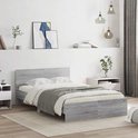 Een grijs eiken houten bed met witte lakens en grijze deken, naast nachtkastjes in een slaapkamer.