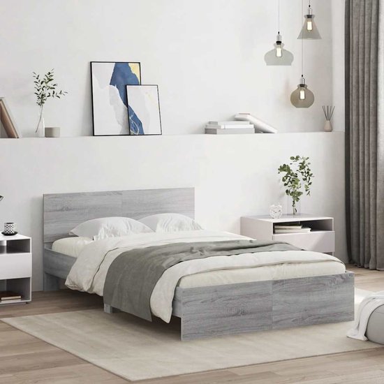 Een grijs eiken houten bed met witte lakens en grijze deken, naast nachtkastjes in een slaapkamer.