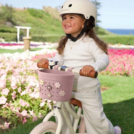 Een jong meisje met een witte helm op een witte fiets met een roze mandje met bloemen.
